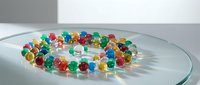 Colorful translucent beads arranged in circle on glass surface, casting vibrant shadows. Suitable for design, jewelry, craft, and educational materials.