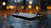 Empty wooden swing suspended by chains in heavy rain with warm bokeh lights in blurred background, suitable for melancholy, loneliness, and emotional storytelling concepts.