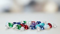 Colorful collection of precious gemstones including emeralds, sapphires, rubies and diamonds scattered on neutral surface for jewelry making and luxury design.
