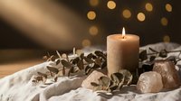 Spa wellness scene with burning candle, eucalyptus leaves and stones on soft fabric with warm bokeh lights creating relaxing atmosphere for meditation.