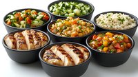 Grilled chicken breast slices served with variety of side dishes including rice, vegetable stew and fresh salads in black ceramic bowls, restaurant menu setup.