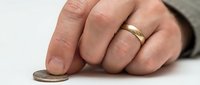 Man wearing gold wedding band holding coin, financial planning and savings concept for business and investment themes.