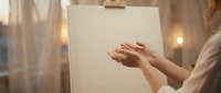 Young woman artist painting on blank canvas with brush in cozy studio with warm lighting. Creative process and artistic expression concept.