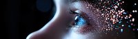 Close up view of woman's eye with glowing blue iris and shimmering pink and gold glitter makeup effect creating magical ethereal beauty look.