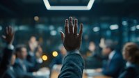 Business professional raising hand during corporate meeting or conference presentation in modern office environment with colleagues in background.