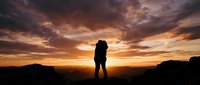 Silhouette of couple embracing on mountain ridge at golden sunset with dramatic sky, romantic outdoor landscape for travel and relationship themes.