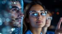 Young Asian female professional in glasses analyzing digital data visualization with glowing blue interface reflection, working on cybersecurity solutions.