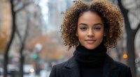 Young African American woman with natural curly hair wearing black turtleneck sweater smiling confidently on urban street with soft bokeh background in autumn.