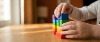 Child hands stacking colorful wooden blocks on a table, building a rainbow tower indoors. Early childhood development and learning through play concept.
