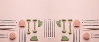 Spa wellness beauty tools jade rollers gua sha stones arranged symmetrically on pink background for skincare routine and facial massage therapy.
