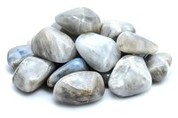 Polished moonstone crystals and tumbled stones in pile showing iridescent blue flash and white pearly luster on white background, isolated for design use.