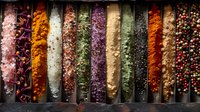Colorful spices and seasonings arranged in rows, vibrant ground powders and peppercorns in dark containers create striking culinary composition. Food ingredients background.