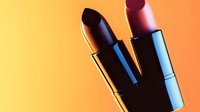 Vibrant close up of two lipsticks casting dramatic shadows on orange and yellow gradient background. Cosmetic beauty product photography with modern minimal style.