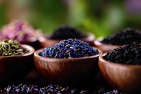 Dried lavender buds and herbal tea ingredients in wooden bowls against dark background, selective focus on aromatic purple flowers for wellness and spa.