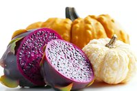 Fresh dragon fruit slices with vibrant magenta flesh displayed alongside orange and white decorative pumpkins on white background, autumn harvest produce arrangement.