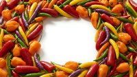 Colorful hot chili peppers arranged in circular wreath pattern on white background. Spicy vegetables frame for cooking, food design and culinary projects.