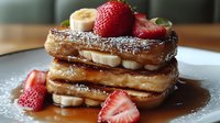 French toast layered with fresh banana slices and strawberries, dusted with powdered sugar and drizzled with maple syrup on white plate, close up view.