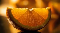 Fresh orange slice with vibrant pulp and juice droplets on warm golden background for healthy eating and citrus fruit concepts.