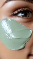 Close-up of green clay mask on female face with long eyelashes and hazel eye, showcasing skincare and beauty treatment application on smooth skin.