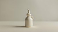 Minimalist white ceramic bottle with elongated spout on neutral beige background. Clean modern composition with soft shadow creates serene atmosphere.