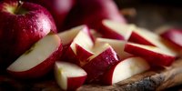 Fresh red apple slices on rustic wooden surface with water droplets, showcasing crisp white flesh and vibrant skin for food photography and healthy eating concepts.