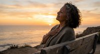 Mature African American woman enjoying peaceful sunset moment on coastal bench, expressing gratitude and mindfulness during golden hour by ocean.