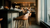 Modern bar stool with wooden seat in upscale restaurant or lounge interior with blurred background, suitable for hospitality and interior design projects.