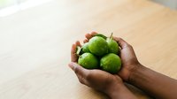 Hands holding fresh green limes on wooden surface, suitable for food, nutrition, cooking, and healthy lifestyle content.