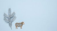 Frosted evergreen branch and decorative sheep figurine arranged on pale blue background, suitable for winter holiday greeting cards and seasonal marketing materials.