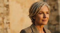 Mature woman with gray hair wearing brown cardigan against warm beige textured wall background. Portrait for lifestyle, aging, professional, and editorial use.