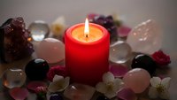 Red candle burning surrounded by colorful healing crystals and gemstones creating peaceful meditation atmosphere for spiritual wellness practices.