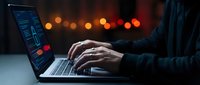 Programmer coding on laptop computer in dark room with colorful bokeh lights background. Software developer working late night on programming project.