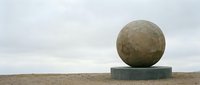 Large stone sphere balanced on concrete platform in barren landscape under overcast sky, representing balance, stability, and minimalist outdoor sculpture art.