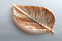 Metallic rose gold leaf brooch with delicate vein details and textured surface on light gray background, macro photography showing fine craftsmanship.