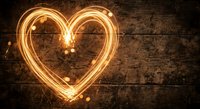 Glowing heart shape made with light trails on rustic wooden background for romantic designs and Valentine's Day projects.