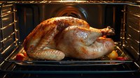 Golden brown roasted whole turkey with crispy skin cooking in oven with vegetables on baking tray, traditional holiday dinner preparation.
