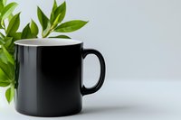 Black ceramic mug on white background with green plant leaves, minimalist composition for mockup design and branding presentations.
