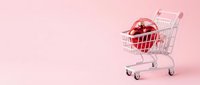 Shopping cart filled with red heart on pink background, symbolizing love-based consumer choices and romantic gift purchasing for Valentine's Day promotions and retail marketing campaigns.