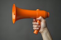 Hand holding bright orange megaphone against dark gray background, demonstrating announcement and communication concept for business and marketing use.
