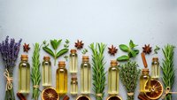 Essential oils in glass bottles with fresh herbs, spices and dried citrus on white background for aromatherapy and natural wellness products.
