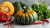Fresh autumn pumpkin with striped green-orange pattern, surrounded by corn, red bell peppers, chili peppers, zucchini and parsley on gray background.