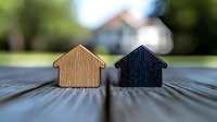 Contrasting light and dark wooden house shapes on textured surface with blurred background, representing real estate, property choice, or housing market concepts.