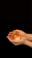 Hands holding glowing amber crystal ball against dark background, symbolizing fortune telling, spirituality, and mystical energy for divination concepts.