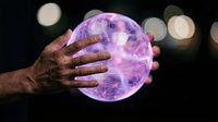 Male hands holding glowing purple energy sphere with electric plasma effects against dark background with bokeh lights for mystical concepts.