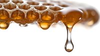 Golden honey dripping from natural honeycomb with hexagonal cells on white background, organic sweetener and healthy food ingredient for culinary use.