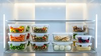 Organized refrigerator shelves displaying various meal prep containers with fresh vegetables, salads, proteins and beverages for weekly food planning and healthy eating routines.