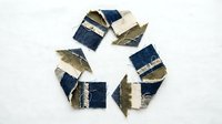 Recycling symbol made from torn denim fabric pieces and gold leaf accents on white background, representing sustainable fashion and environmental awareness for eco-friendly design projects.
