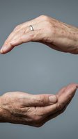 Elderly hands forming protective gesture showing care and security concept for healthcare insurance and senior support services.