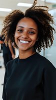 Young African American woman with natural curly hair and bright smile wearing black casual top in office setting, expressing joy and confidence at workplace.