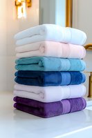 Stack of colorful cotton bath towels neatly folded in modern bathroom interior for home decor and hospitality industry marketing materials.